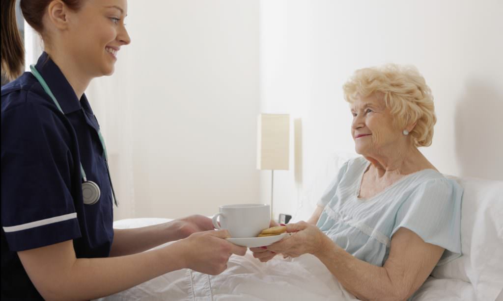 nurse giving tea to an old woman in bed